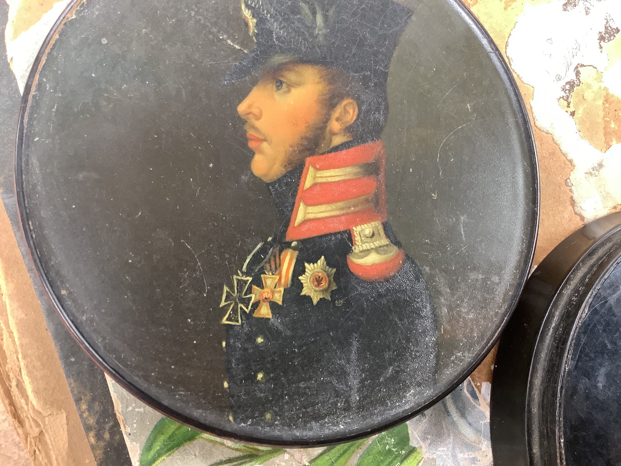 A 19th century Stobwasser papier mache ‘Henriette Sonntag’ portrait snuff box, c.1830, 9.7cm diameter and a 19th-century papier mache snuff box painted with a portrait of a German hussar, 9.4cm (2)